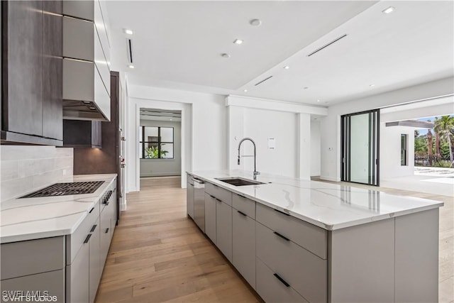 kitchen with modern cabinets, a sink, gray cabinetry, a spacious island, and light wood finished floors