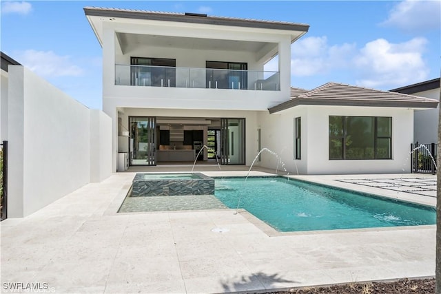 back of house with a patio area, a balcony, an in-ground hot tub, and stucco siding