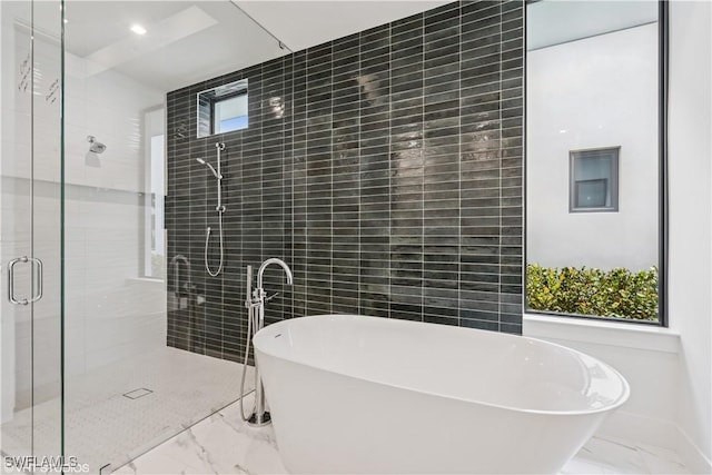 bathroom with marble finish flooring, a shower stall, a soaking tub, and tile walls
