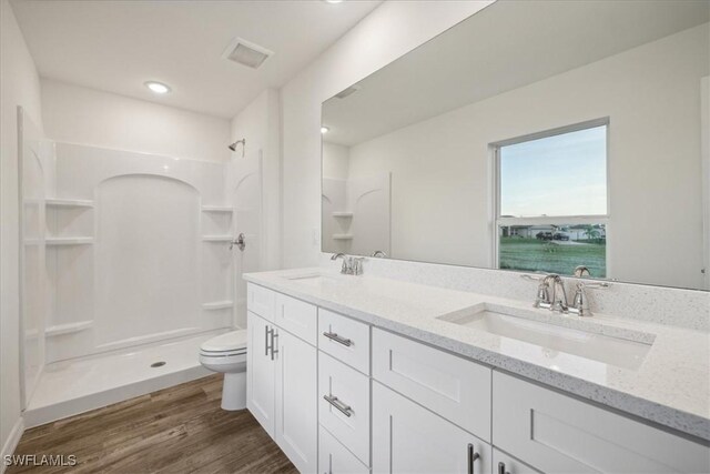 bathroom featuring toilet, walk in shower, wood finished floors, double vanity, and recessed lighting