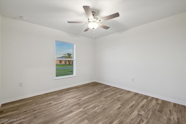 empty room with wood finished floors, a ceiling fan, baseboards, and a smoke detector
