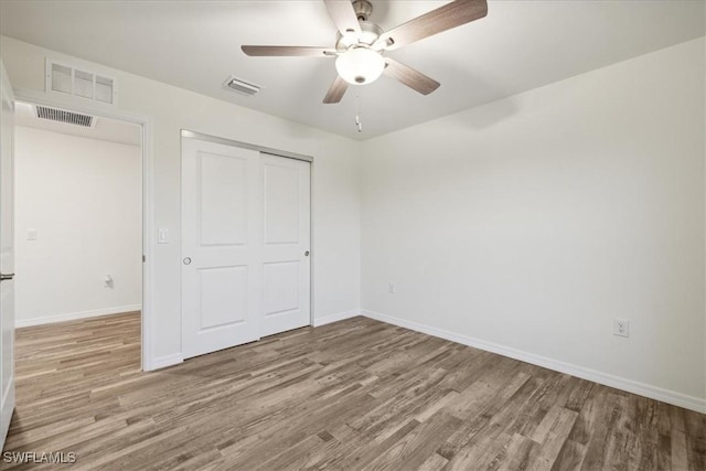 unfurnished bedroom with wood finished floors, a closet, baseboards, and a ceiling fan