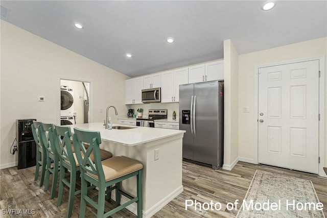 kitchen with appliances with stainless steel finishes, stacked washer / drying machine, a sink, light wood-type flooring, and vaulted ceiling