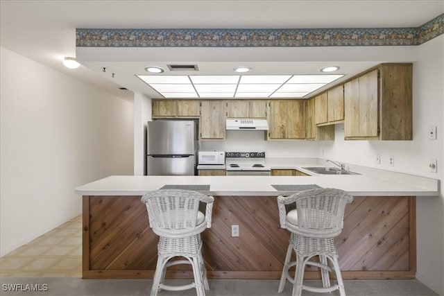 kitchen with white appliances, a sink, under cabinet range hood, a peninsula, and light countertops