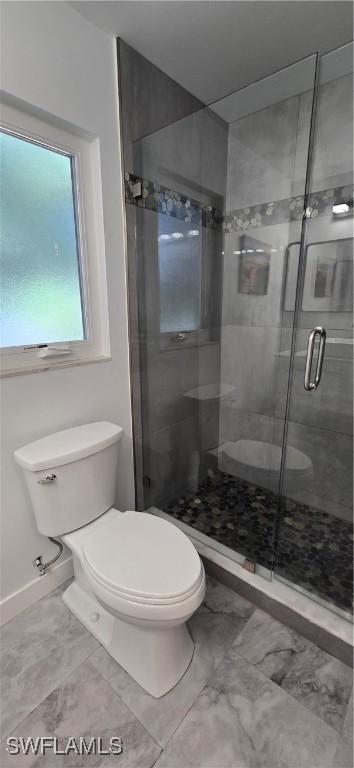 full bath with toilet, a stall shower, and baseboards