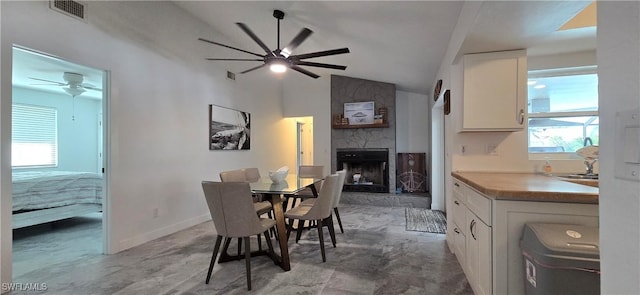 dining space featuring ceiling fan, a fireplace, vaulted ceiling, and baseboards