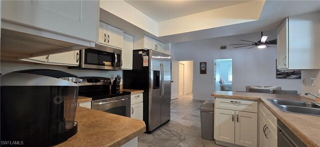 kitchen featuring stainless steel appliances, a sink, a peninsula, and white cabinetry