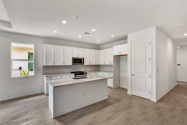 44311 Panther Dr, Punta Gorda, FL 33982 - kitchen featuring stainless steel microwave, a sink, light wood-style floors, white cabinets, and tasteful backsplash