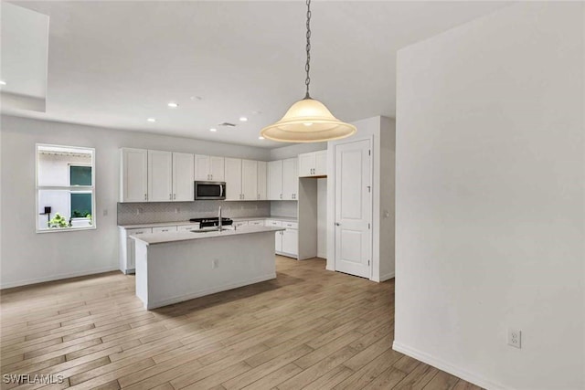 44311 Panther Dr, Punta Gorda, FL 33982 - kitchen with stainless steel microwave, white cabinetry, baseboards, light countertops, and light wood-type flooring