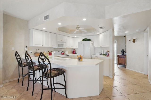 1020 S Collier Blvd Unit 402, Marco Island, FL 34145 - kitchen with white appliances, a peninsula, light tile patterned floors, a tray ceiling, and a breakfast bar area