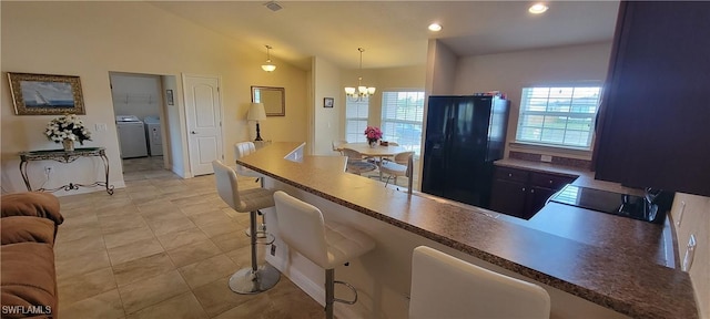 kitchen with black fridge with ice dispenser, washing machine and clothes dryer, a chandelier, lofted ceiling, and hanging light fixtures