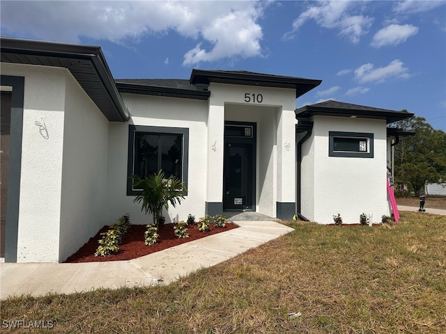 view of exterior entry with stucco siding and a lawn