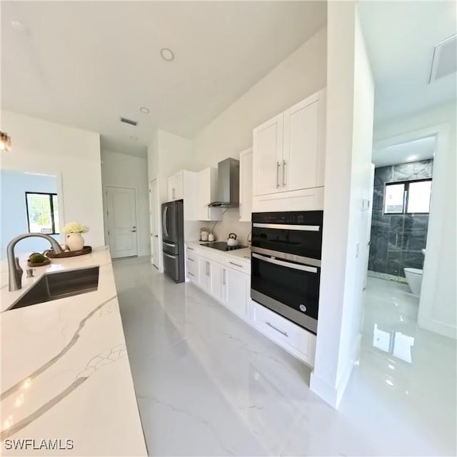 kitchen featuring a sink, wall chimney range hood, black electric cooktop, and white cabinetry