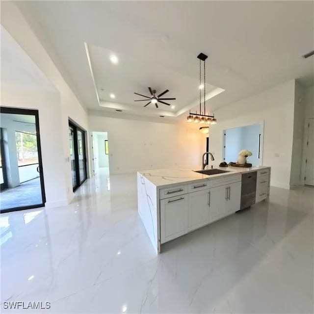 kitchen featuring a sink, a tray ceiling, open floor plan, an island with sink, and dishwashing machine