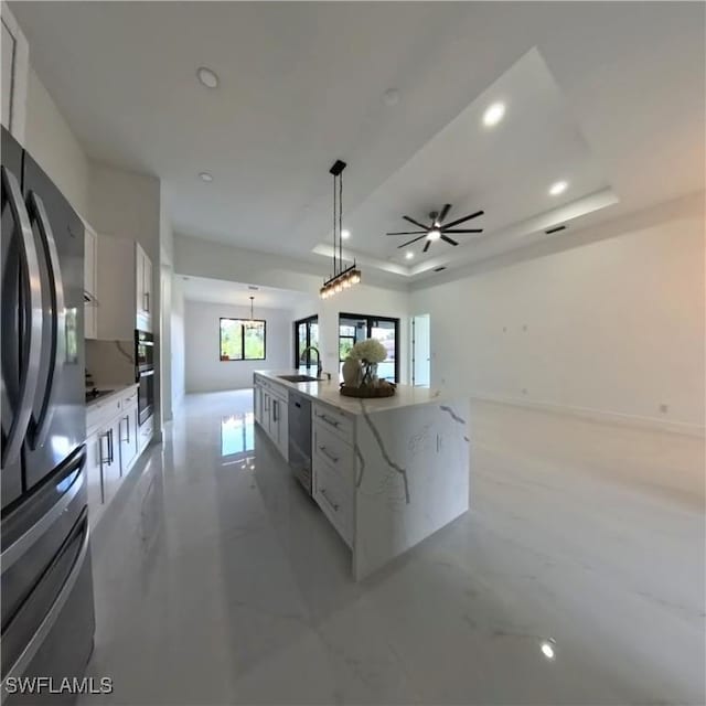 kitchen featuring stainless steel appliances, a sink, white cabinetry, hanging light fixtures, and a large island with sink