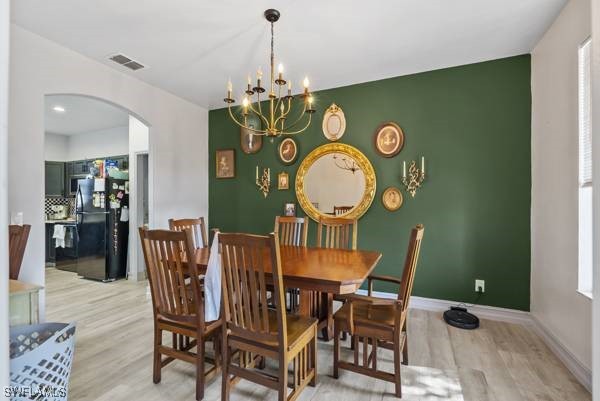 857 Bedford Dr, Lehigh Acres, FL 33974 - dining space with arched walkways, light wood-style floors, a chandelier, baseboards, and an accent wall