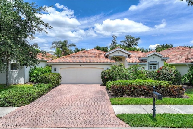 mediterranean / spanish-style house featuring a garage, stucco siding, decorative driveway, and a tiled roof