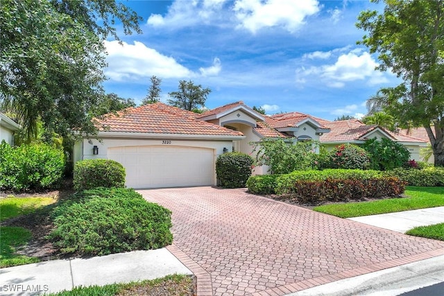 mediterranean / spanish-style home with a garage, decorative driveway, stucco siding, and a tile roof