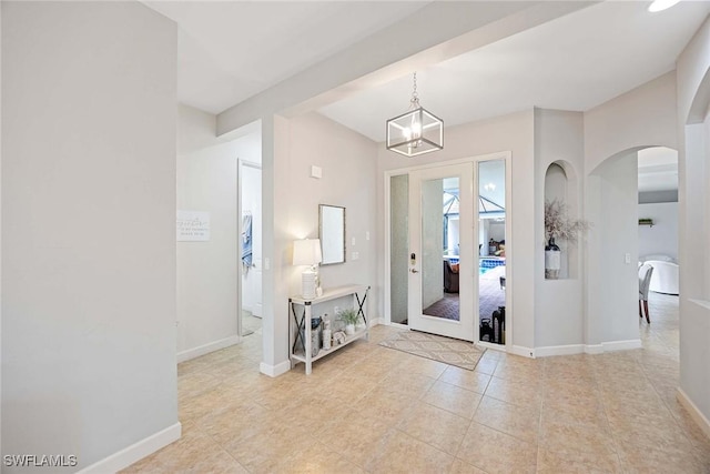 entrance foyer featuring tile patterned flooring, arched walkways, baseboards, and a chandelier