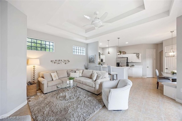 living area with a raised ceiling, a ceiling fan, light tile patterned flooring, recessed lighting, and baseboards