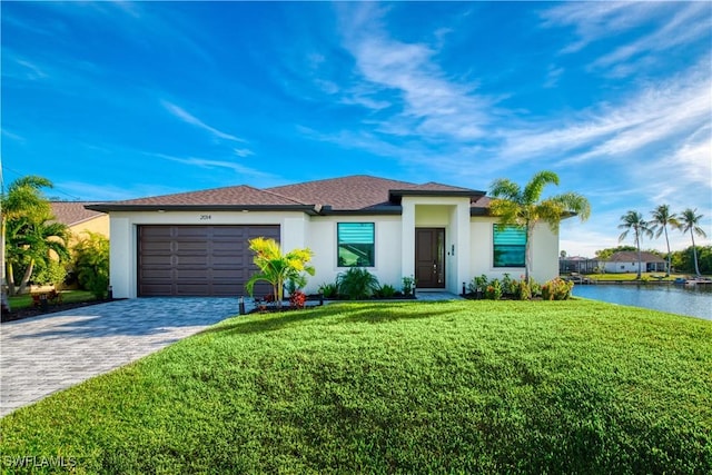 prairie-style home with an attached garage, a front yard, stucco siding, decorative driveway, and a water view