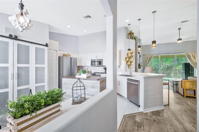 kitchen with stainless steel appliances, white cabinetry, a sink, light wood-style floors, and hanging light fixtures