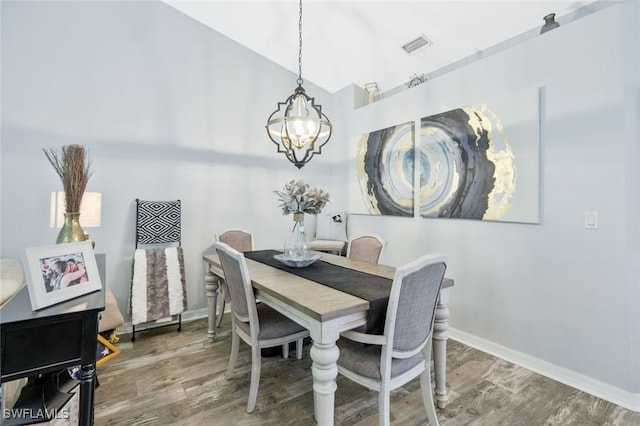 dining room with a chandelier, wood finished floors, baseboards, and lofted ceiling
