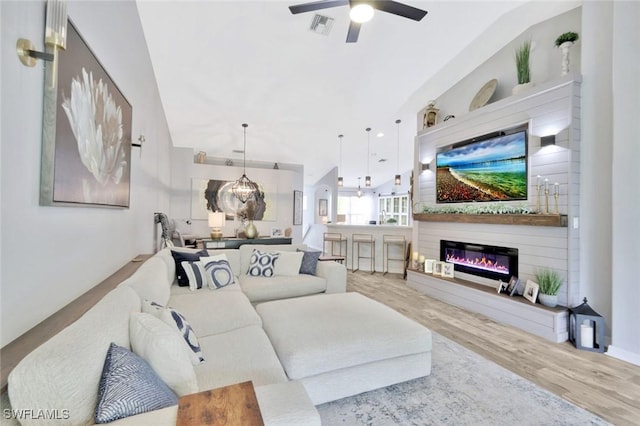 living area featuring a glass covered fireplace, wood finished floors, ceiling fan, and lofted ceiling