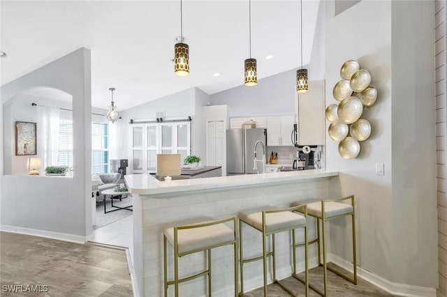 kitchen with freestanding refrigerator, a peninsula, light countertops, white cabinetry, and arched walkways