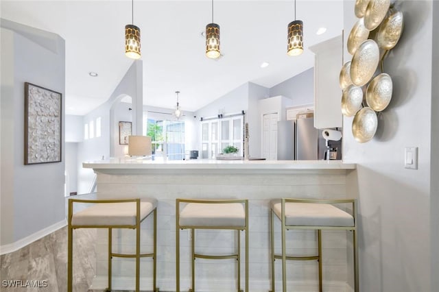kitchen with a breakfast bar area, freestanding refrigerator, a peninsula, vaulted ceiling, and baseboards