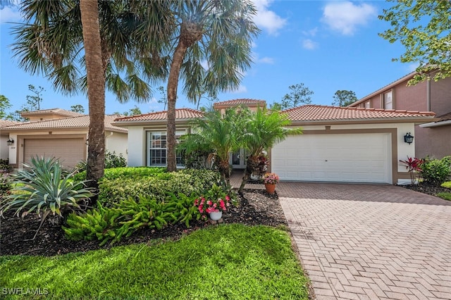 mediterranean / spanish-style home featuring an attached garage, stucco siding, a tiled roof, and decorative driveway