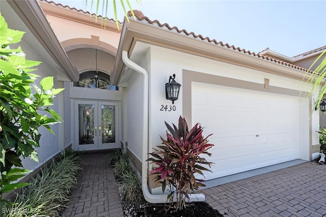 property entrance with french doors, stucco siding, a garage, and decorative driveway