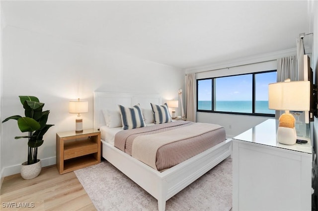 bedroom with light wood-style flooring, a water view, and baseboards