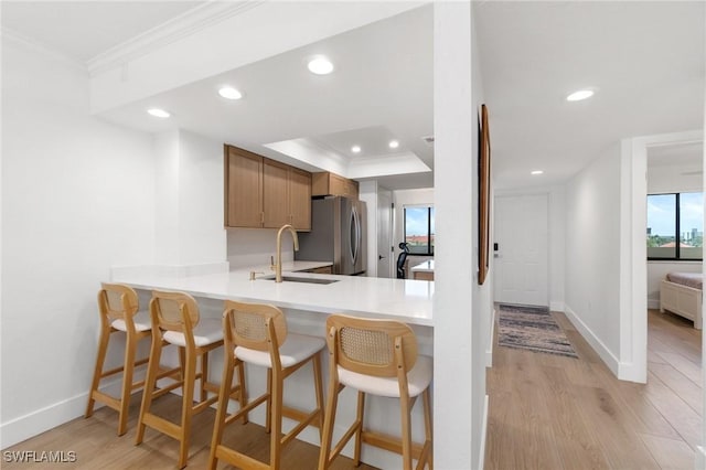 kitchen featuring freestanding refrigerator, a sink, light wood-type flooring, baseboards, and crown molding