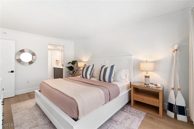 bedroom with light wood-type flooring, crown molding, baseboards, and ensuite bath