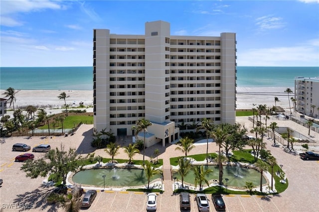 view of apartment building / complex featuring view of water and beach and uncovered parking