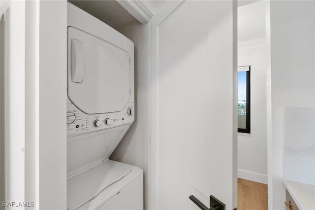 laundry room featuring stacked washer and clothes dryer, light wood-type flooring, and baseboards
