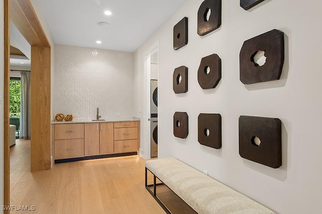 hall featuring estacked washer and dryer, light wood-type flooring, a sink, and recessed lighting