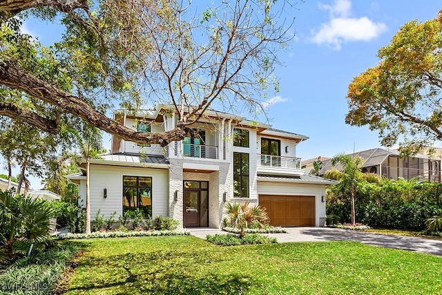 view of front facade featuring a balcony, a standing seam roof, a garage, driveway, and a front lawn