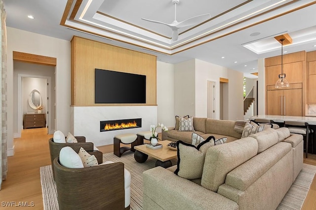 living room with a tray ceiling, a fireplace, light wood-style floors, recessed lighting, and ceiling fan