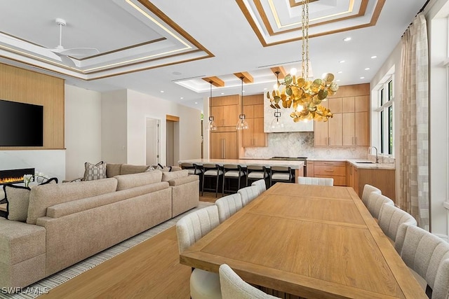 dining space with a raised ceiling, light wood-style floors, recessed lighting, ceiling fan, and a fireplace