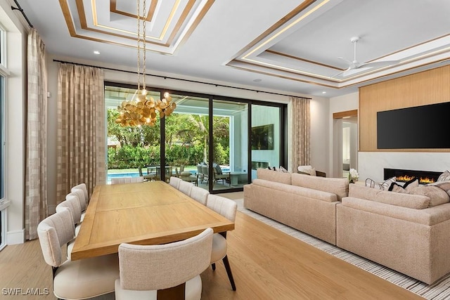 living room featuring a raised ceiling, wood finished floors, a fireplace, recessed lighting, and a chandelier