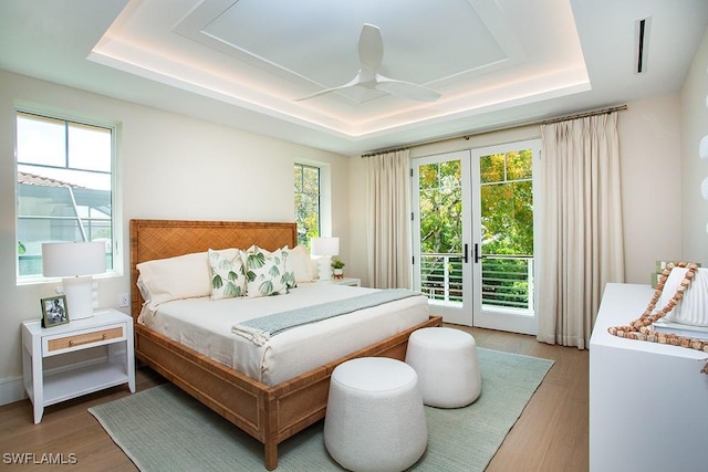 bedroom featuring a raised ceiling, access to outside, french doors, and wood finished floors