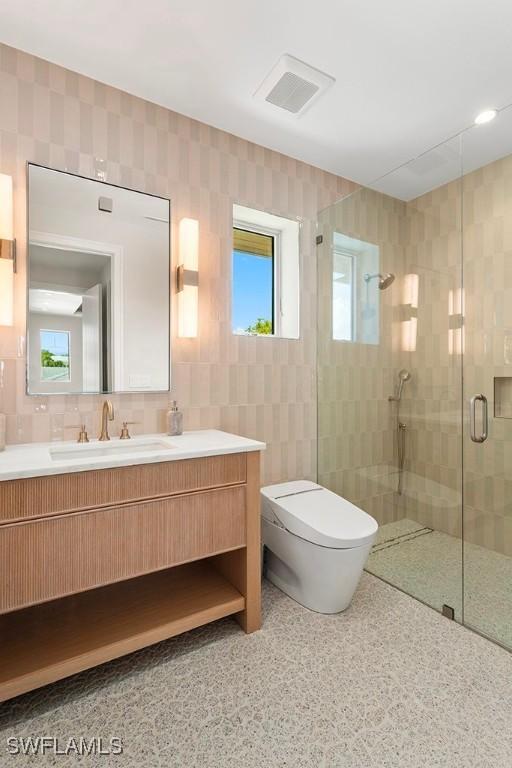 bathroom with a stall shower, toilet, vanity, speckled floor, and tile walls