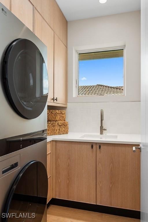 laundry room featuring stacked washing machine and dryer, cabinet space, and light wood-style flooring