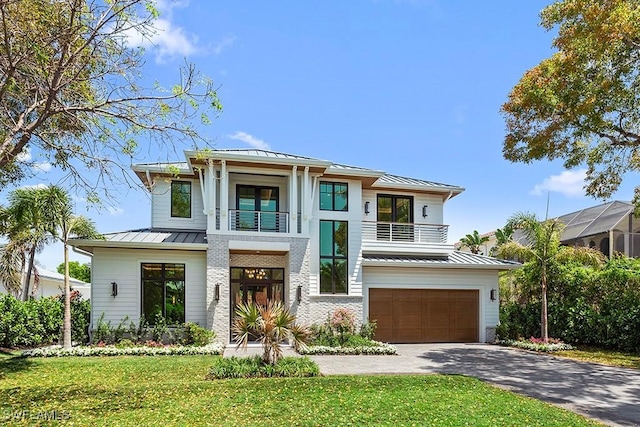 view of front of house featuring a standing seam roof, a balcony, metal roof, a garage, and a front lawn