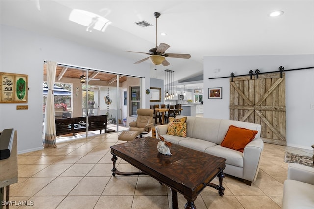 living area with a ceiling fan, a barn door, vaulted ceiling, light tile patterned floors, and baseboards