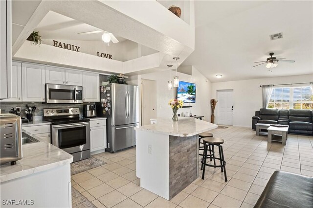 927 NW 12th Ter, Cape Coral, FL 33993 - kitchen featuring stainless steel appliances, ceiling fan, light tile patterned floors, a kitchen bar, and lofted ceiling