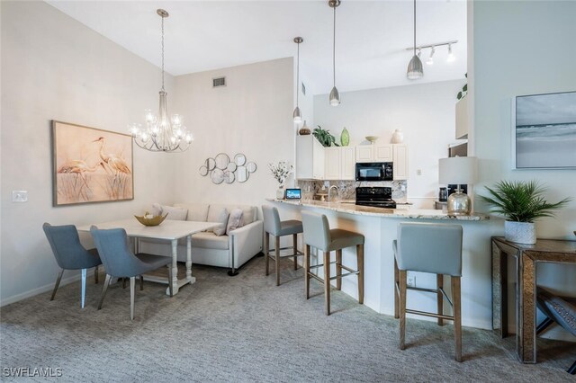kitchen with black appliances, carpet flooring, tasteful backsplash, a breakfast bar area, and a chandelier