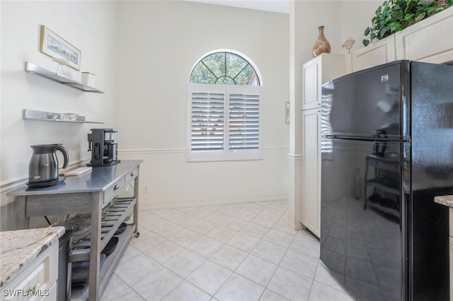 kitchen featuring freestanding refrigerator, wainscoting, light tile patterned floors, light stone counters, and open shelves